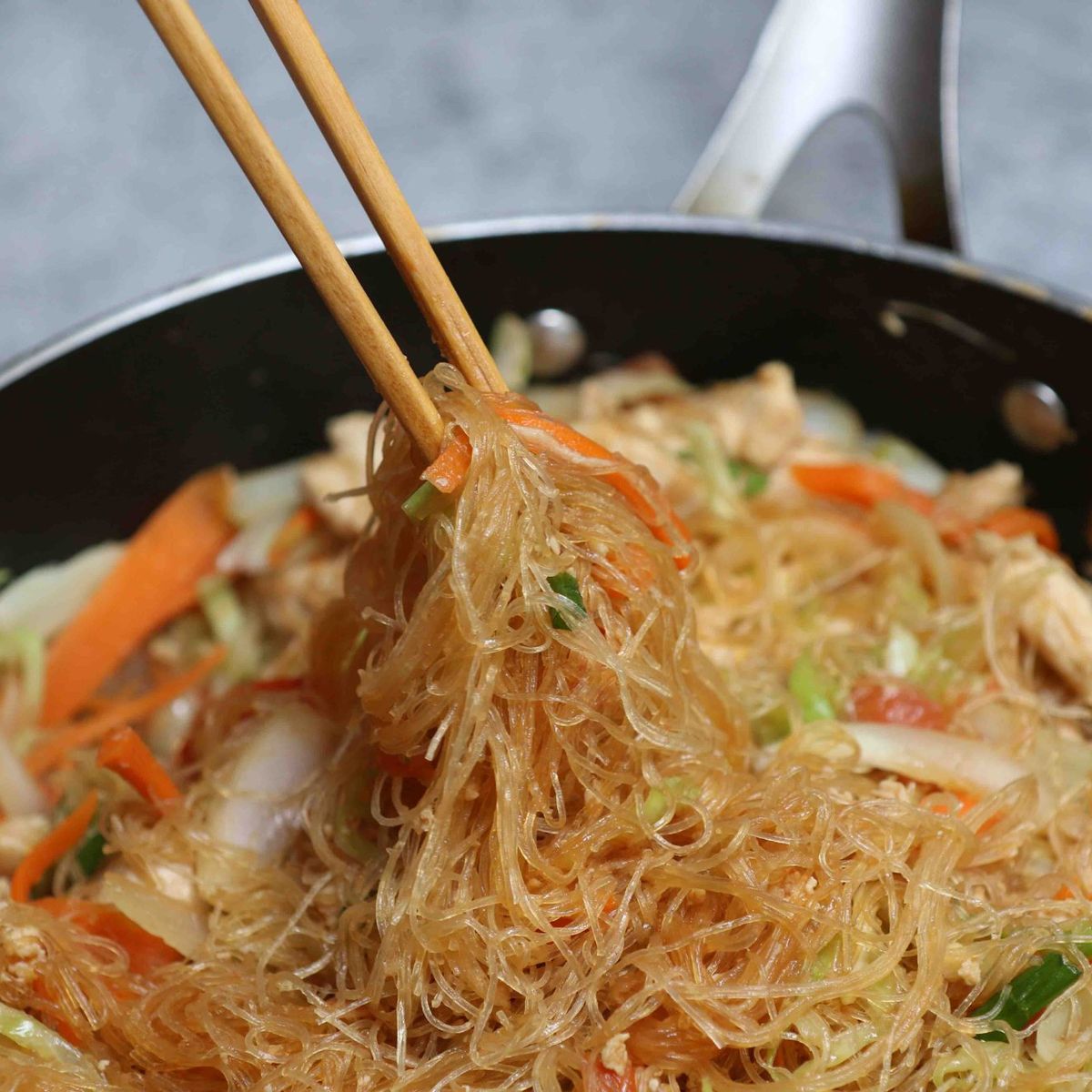Glass noodle stir fry with bean thread noodles, egg, and vegetables in a ceramic bowl with chopsticks