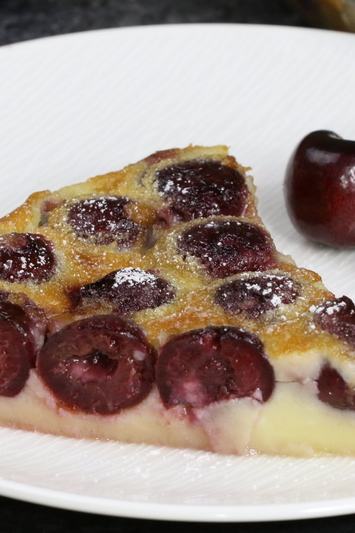 A piece of Clafoutis was cut and served on a white plate
