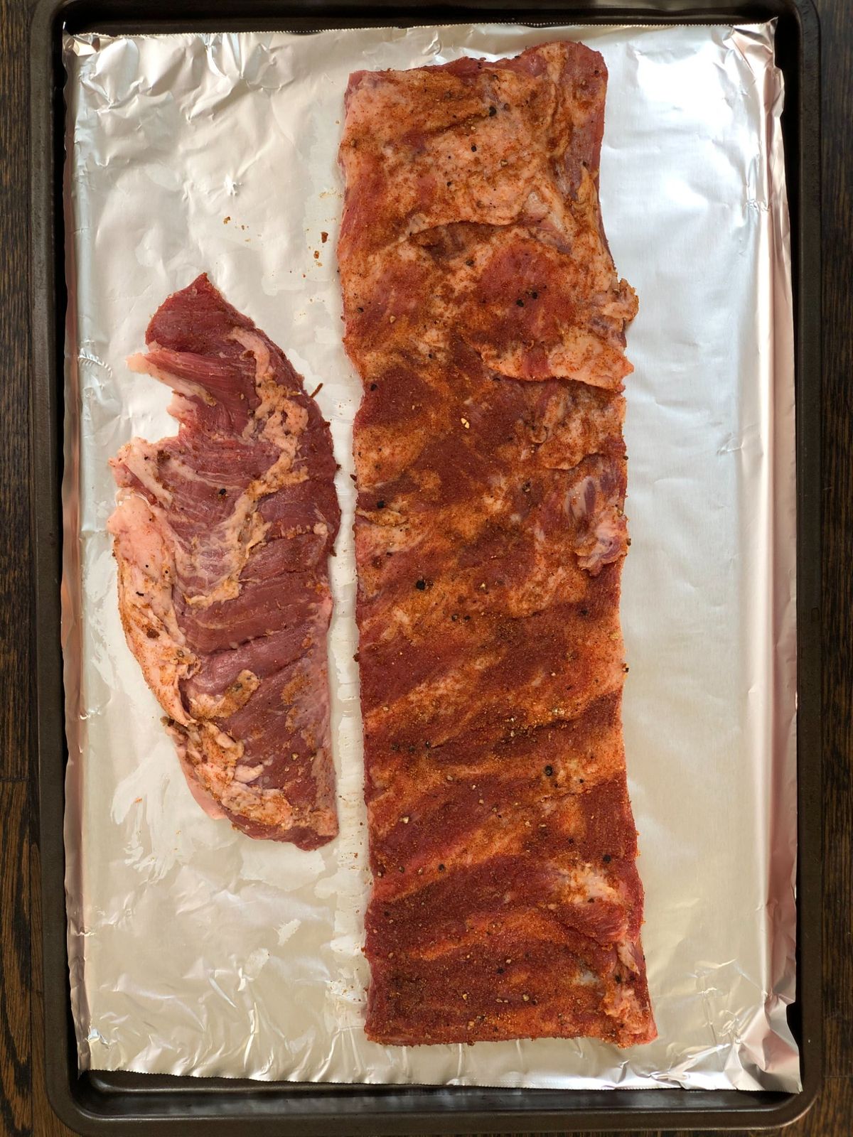 Raw pork ribs coated with dry rub seasoning on a foil-lined baking sheet before baking